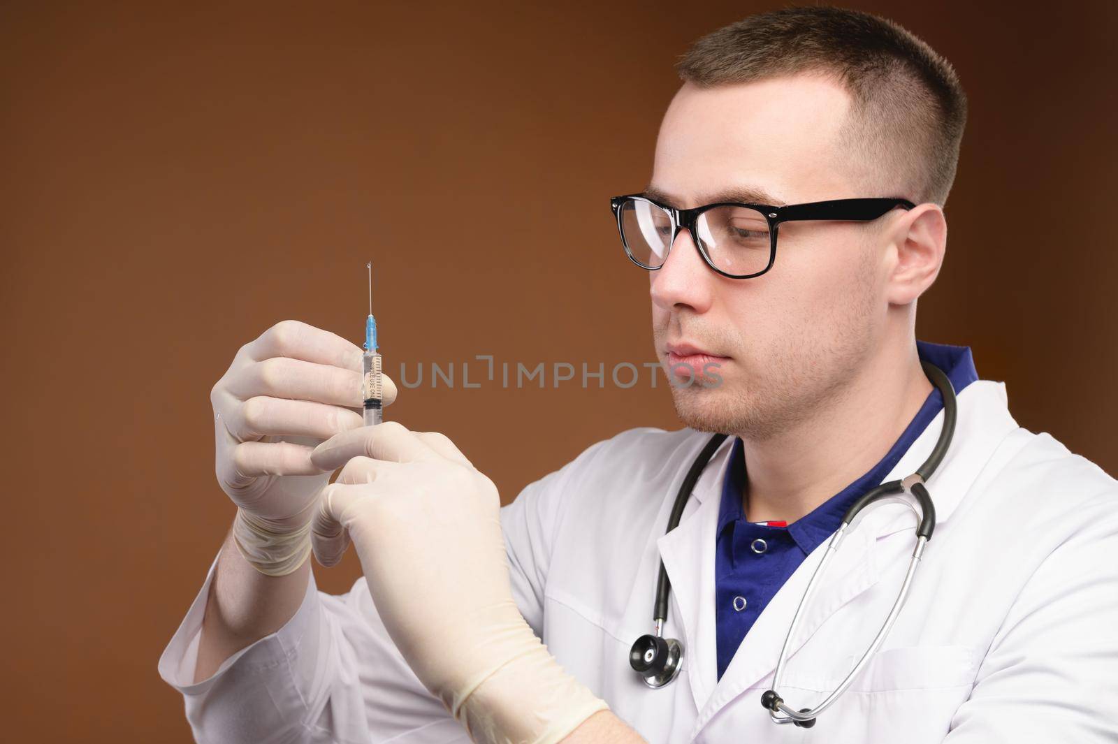 Young caucasian doctor man preparing to do a vaccination with a syringe. Studio shot on a brown background. Release air from the syringe before the injection.