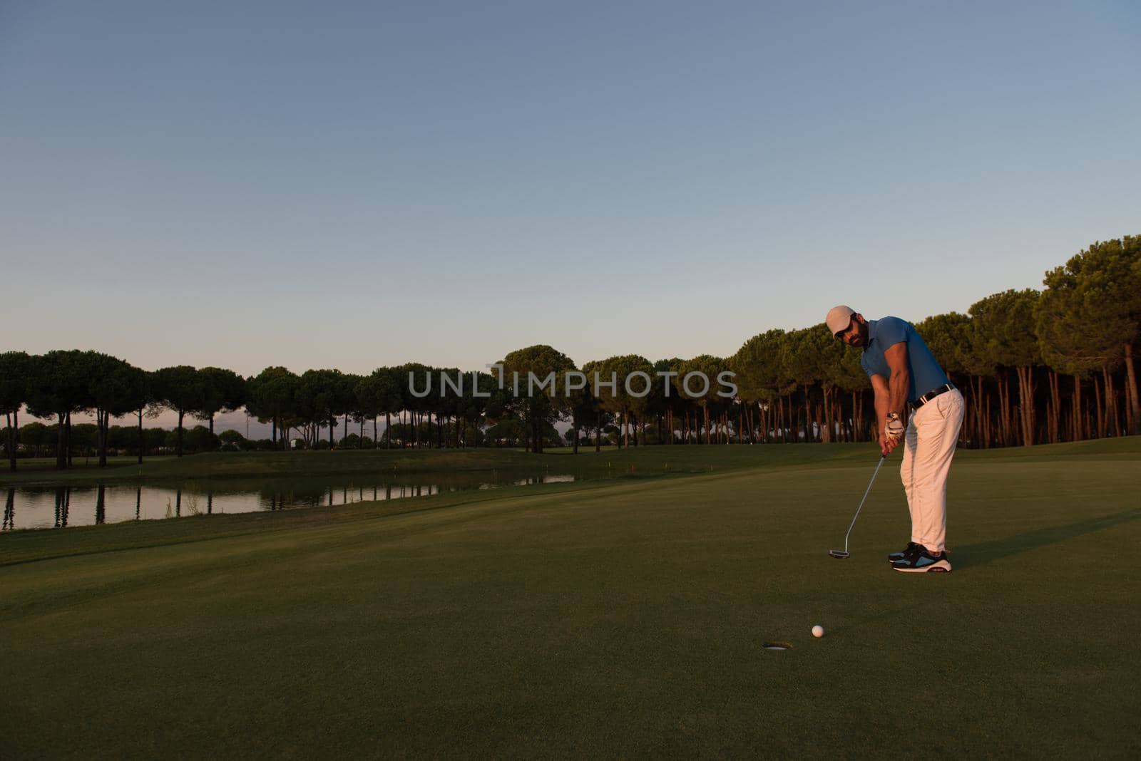 golfer hitting ball shot with driver on golf course at beautiful sunset in background