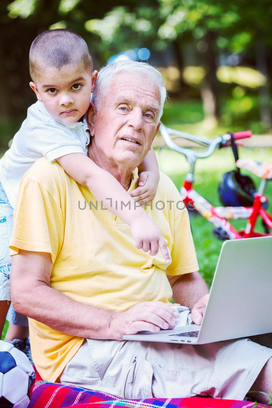 happy elderly senior grandfather and child in park using laptop computer