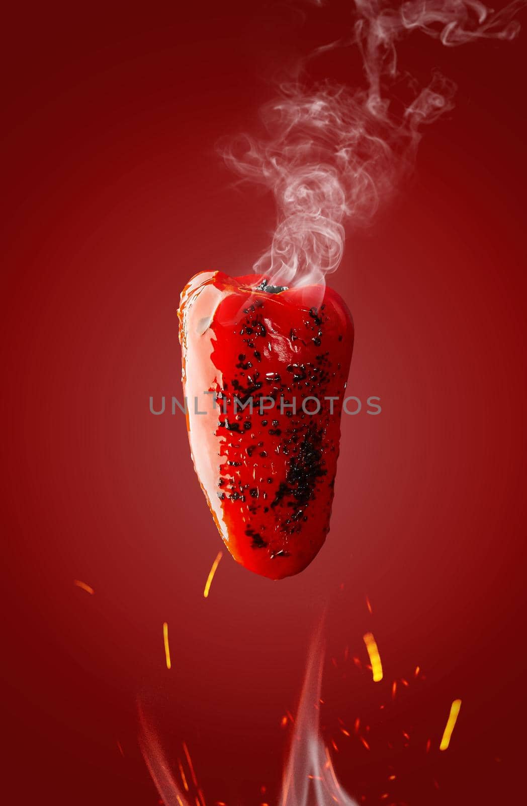 Hot steaming grilled bell pepper hovering over flames with sparks on red background. Food levitation concept
