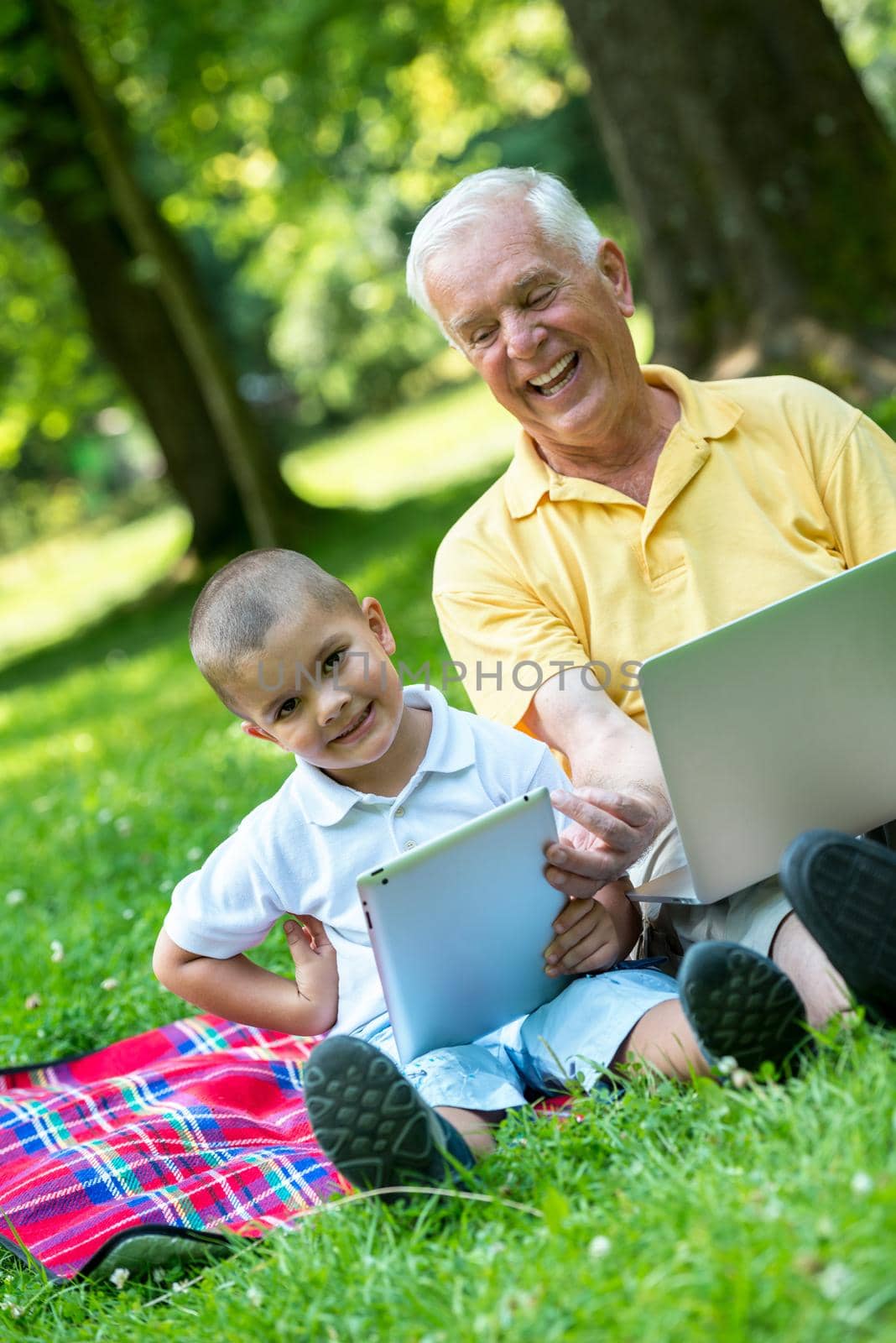 happy elderly senior grandfather and child in park using laptop computer