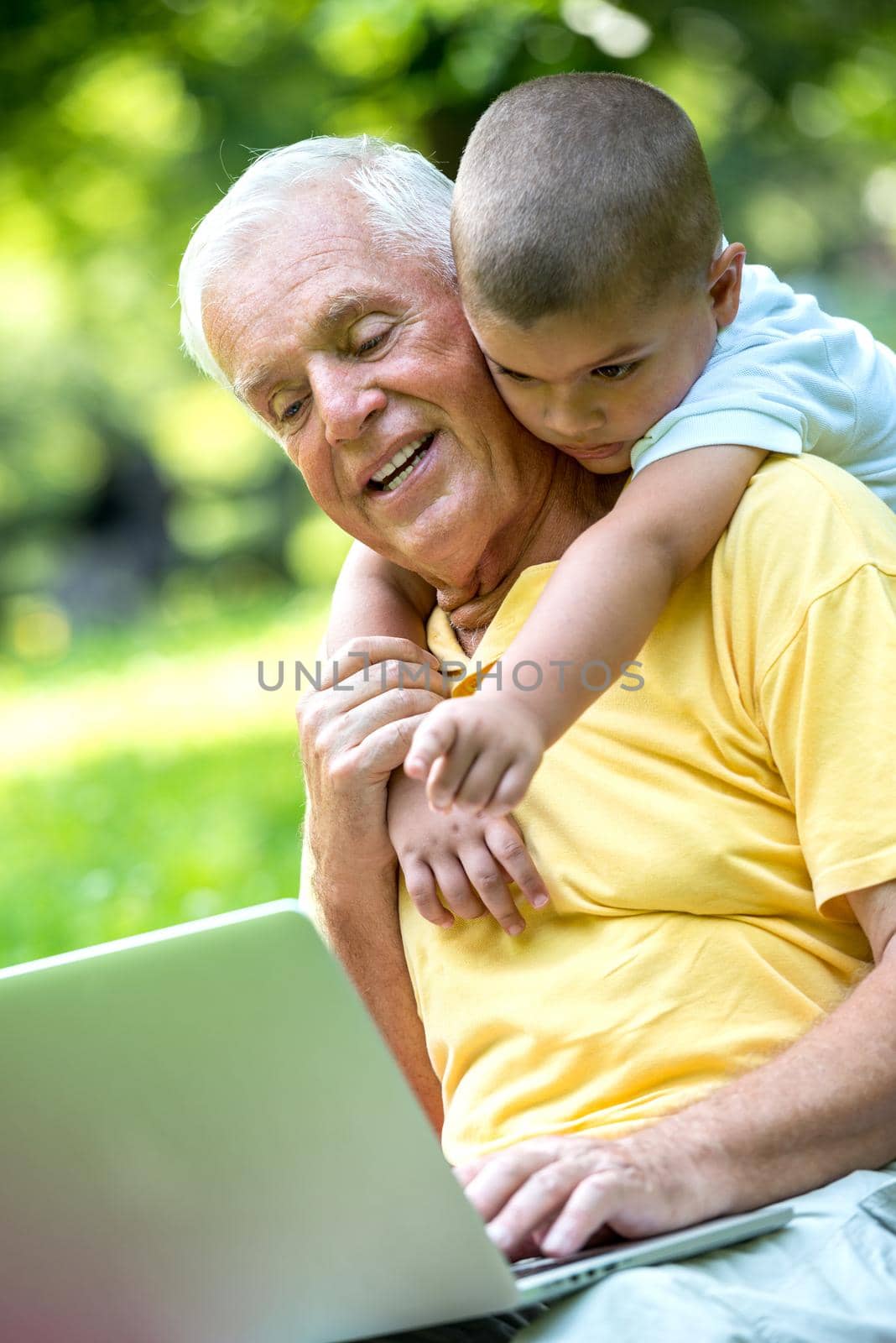 happy elderly senior grandfather and child in park using laptop computer