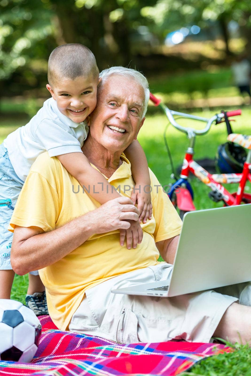 happy elderly senior grandfather and child in park using laptop computer