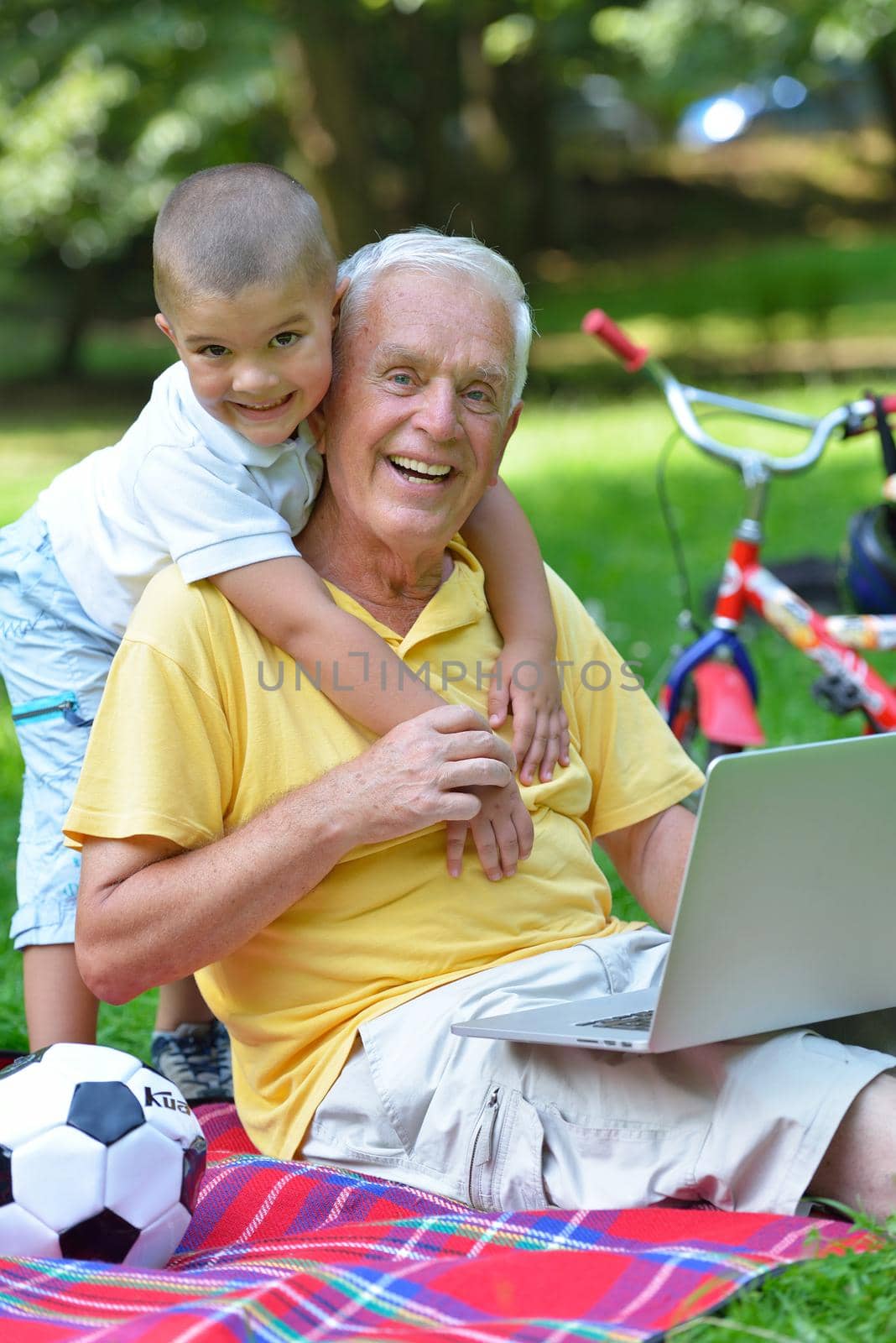 happy elderly senior grandfather and child in park using laptop computer