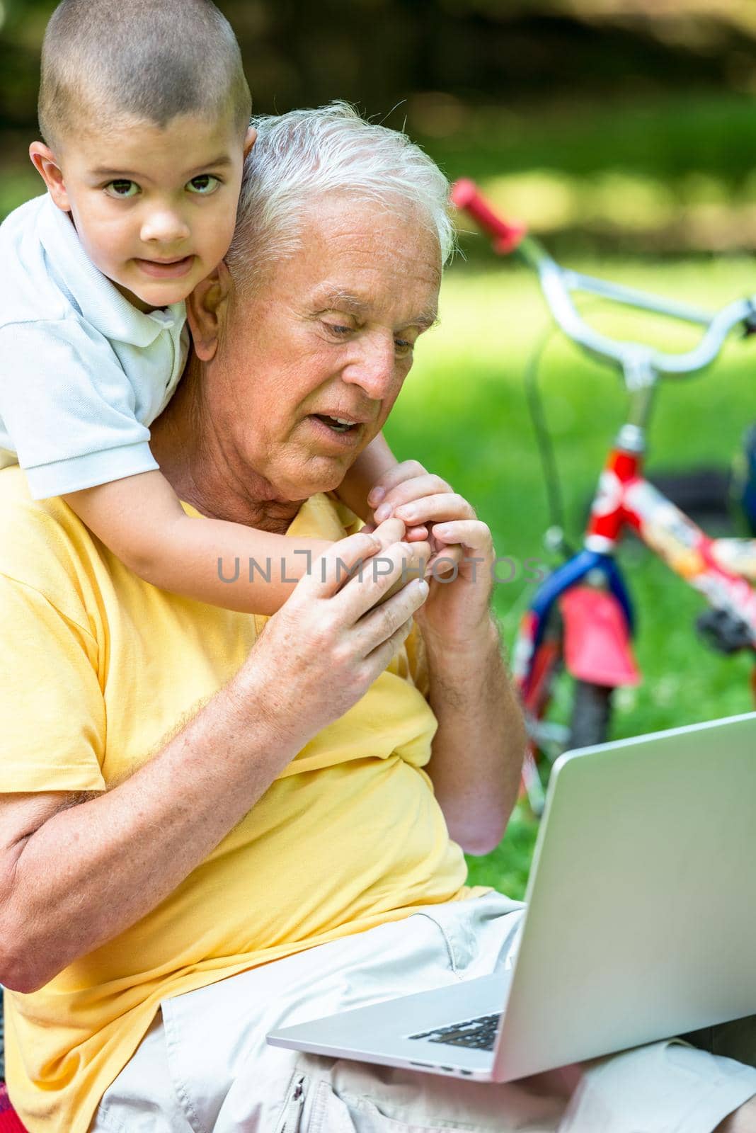 happy elderly senior grandfather and child in park using laptop computer