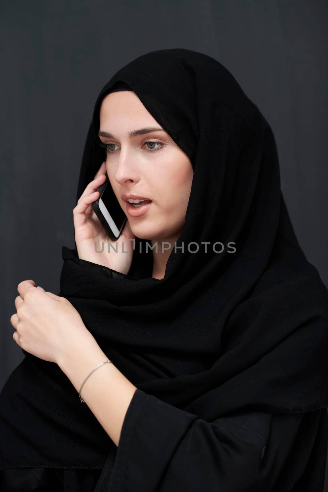 Young muslim businesswoman in traditional clothes or abaya talking on the smartphone. Arab woman  in front of black chalkboard and representing techology, islamic  fashion and Ramadan kareem concept