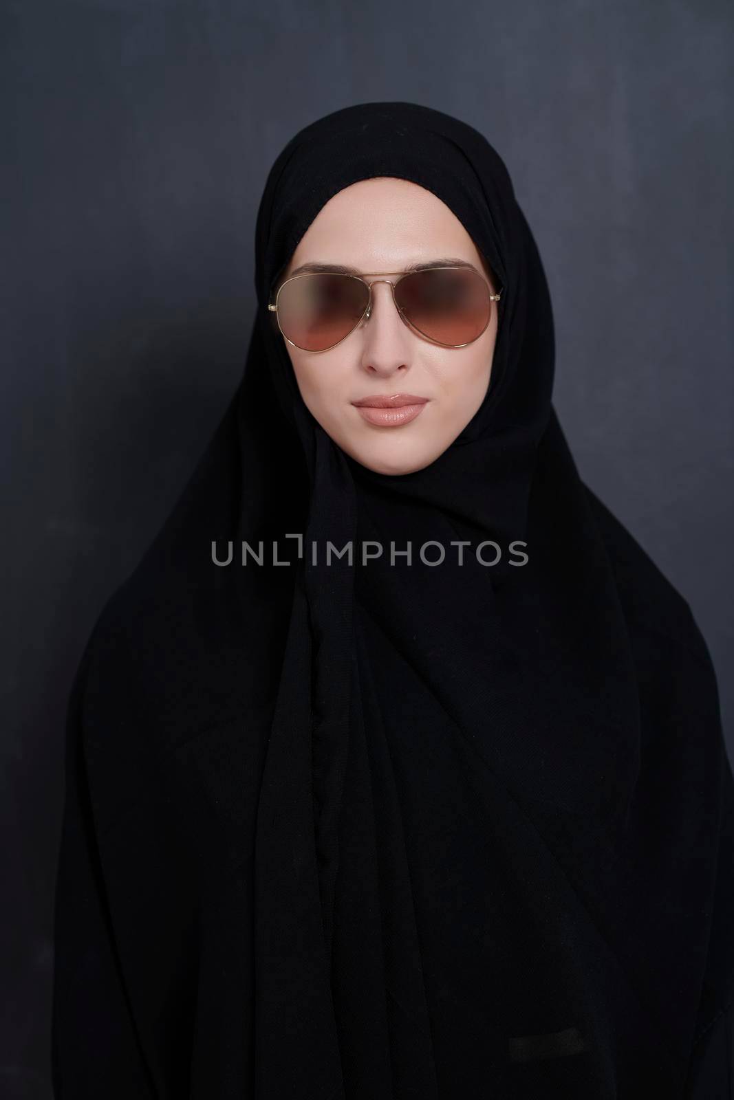 Young muslim businesswoman in traditional clothes or abaya and sunglasses posing in front of black chalkboard. Arab woman representing modern arabic lifestyle, islamic  fashion and Ramadan kareem concept