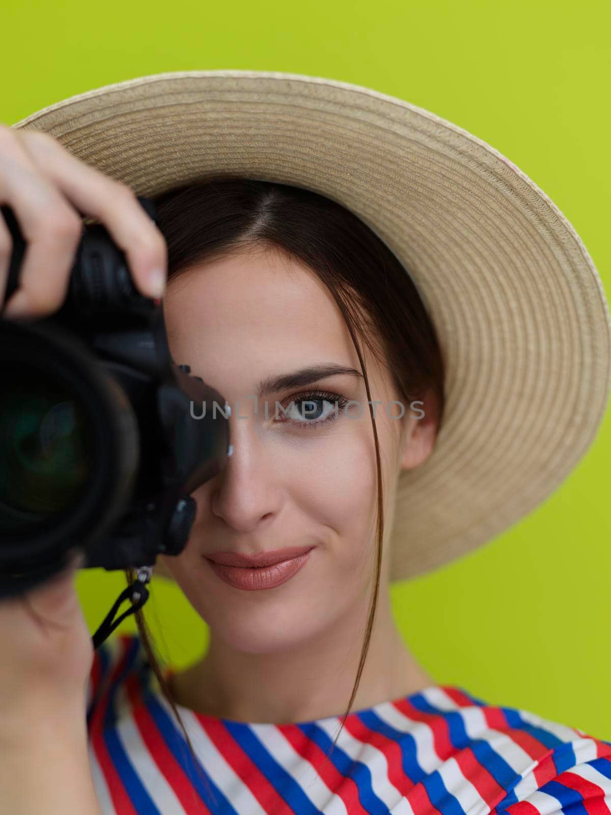 Portrait of beautiful female photographer shooting close up. Say cheese. Young smiling woman holding camera isolated on green background