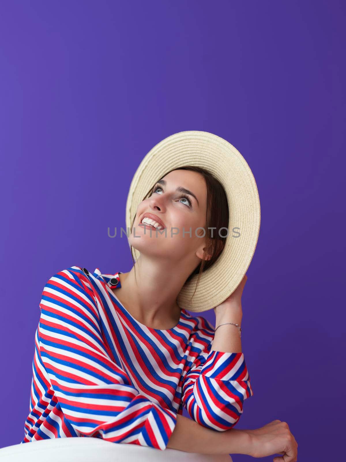 Portrait of young woman sitting on the chair isolated on purple background. Female model in casual and modern clothes posing in the studio