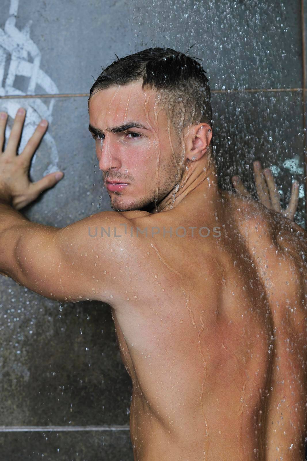 young good looking and attractive man with muscular body wet taking showe in bath with black tiles in background