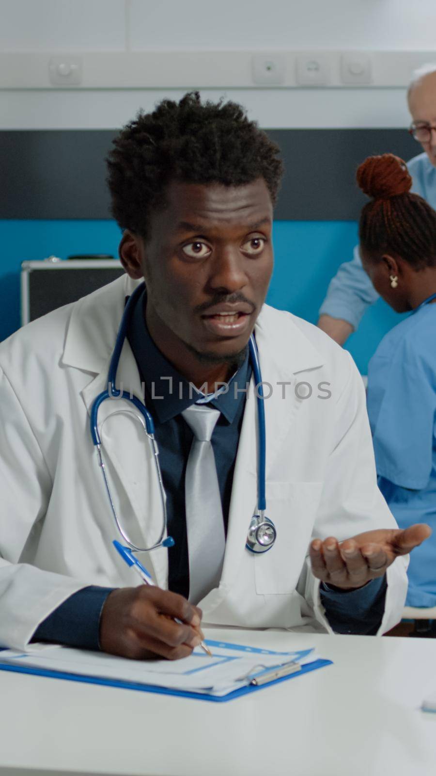 African american doctor consulting sick old woman while sitting at desk in medical cabinet. Senior patient receiving professional advice from young medic wearing uniform and stethoscope