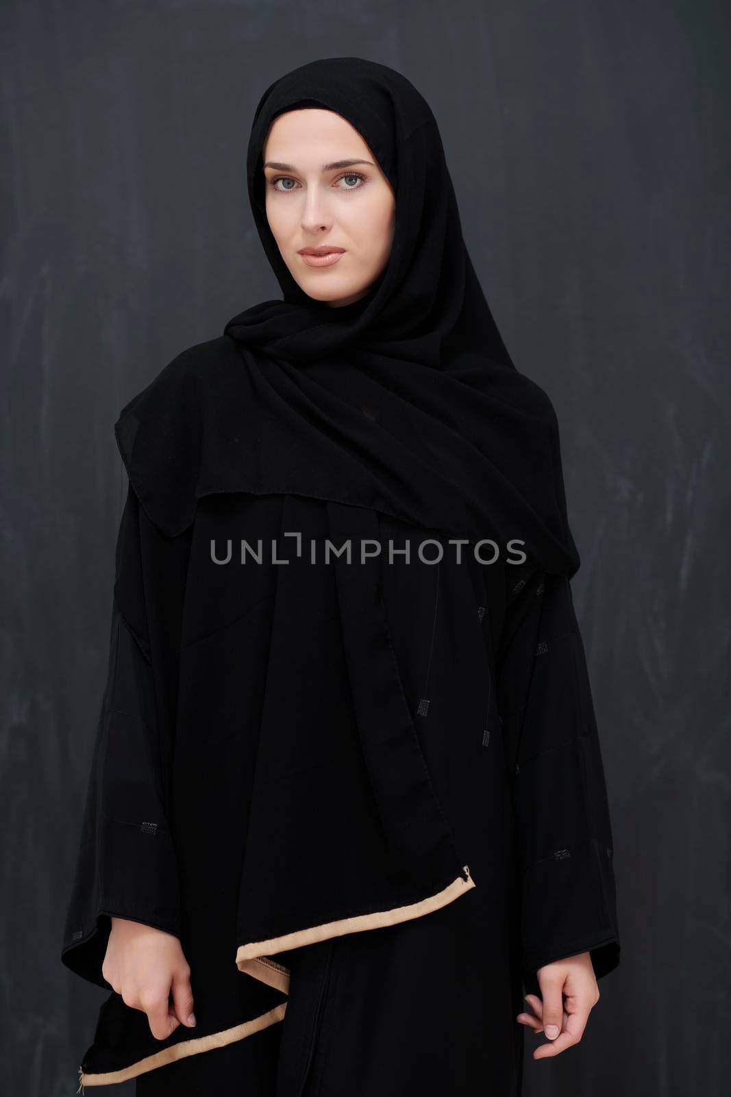 Modern young muslim woman in black abaya. Arab girl wearing traditional clothes and posing in front of black chalkboard. Representing modern and rich arabic lifestyle