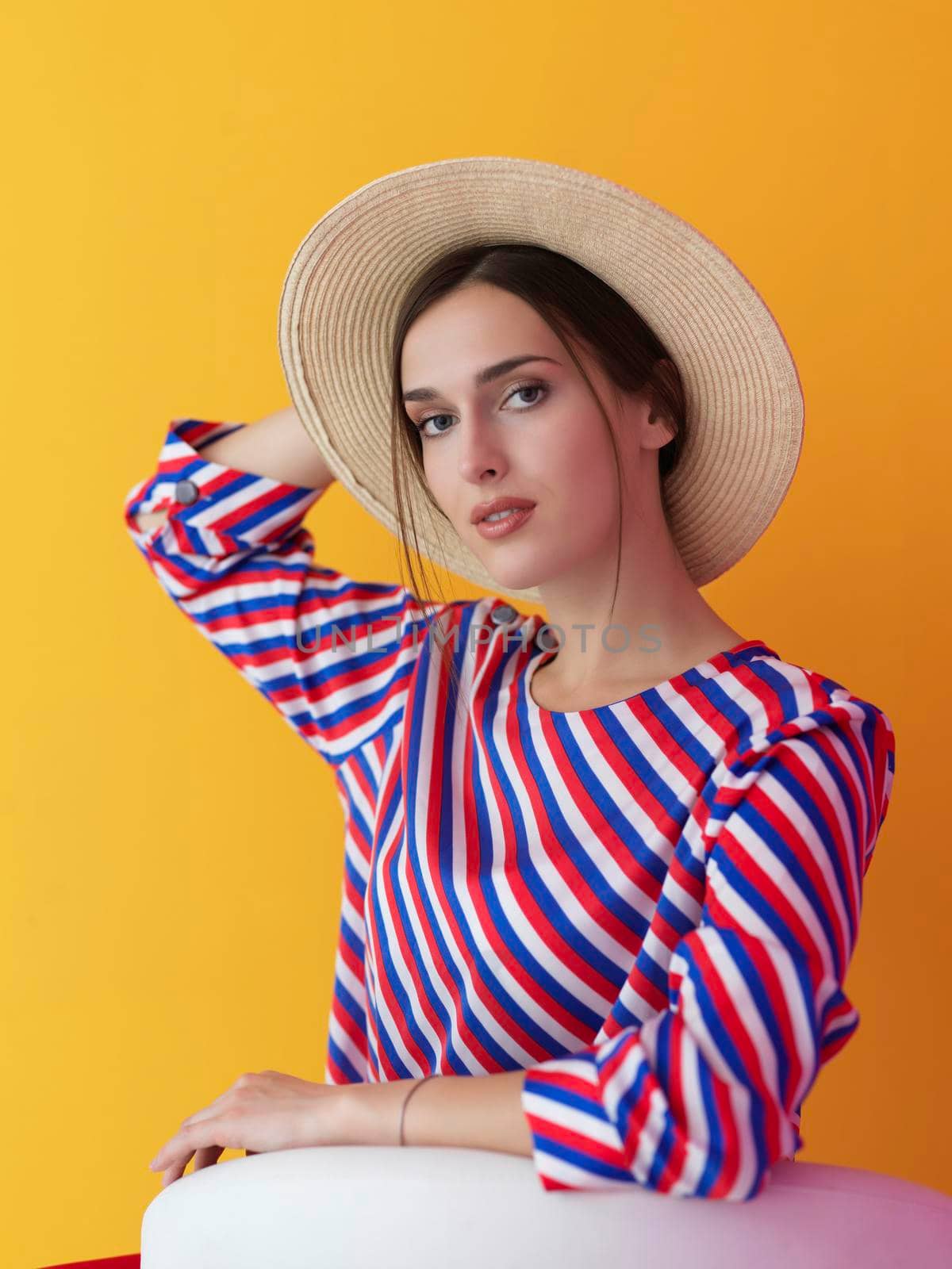 Portrait of young woman sitting on the chair isolated on yellow background. Female model in casual and modern clothes posing in the studio