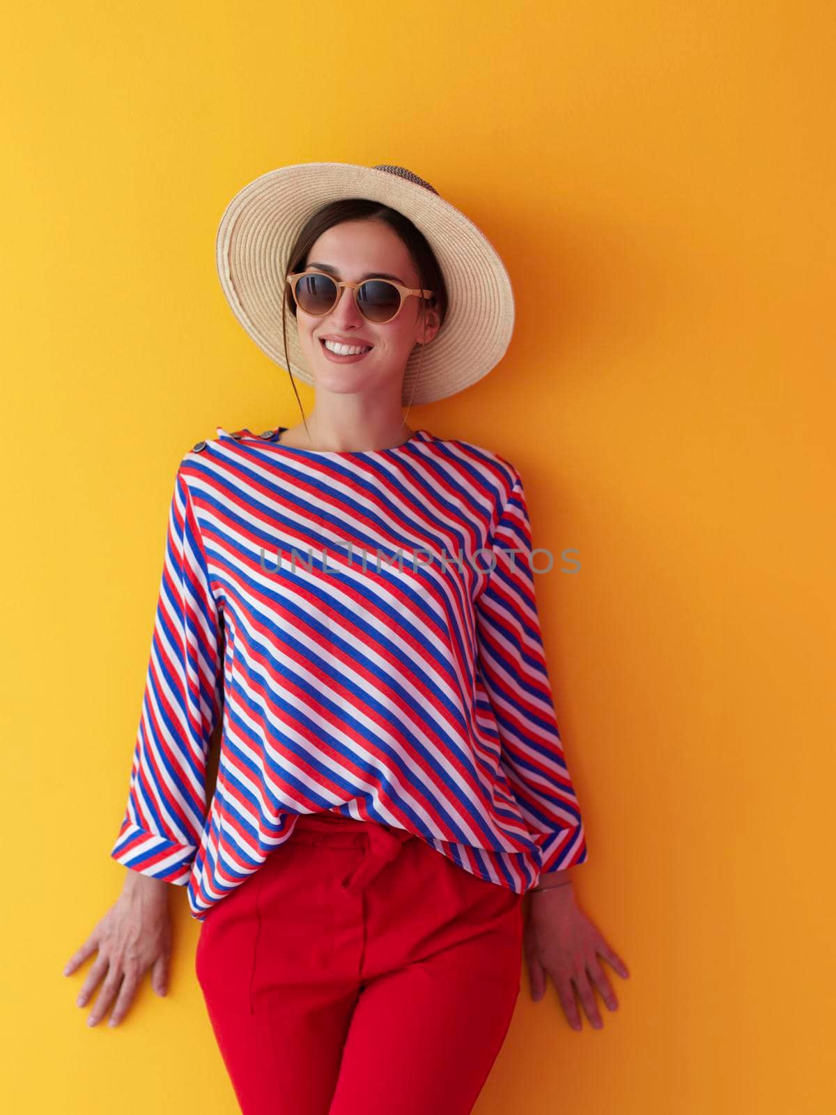 Portrait of young woman wearing sunglasses and hat over a yellow background. Female model posing in the studio. Concept of fashion