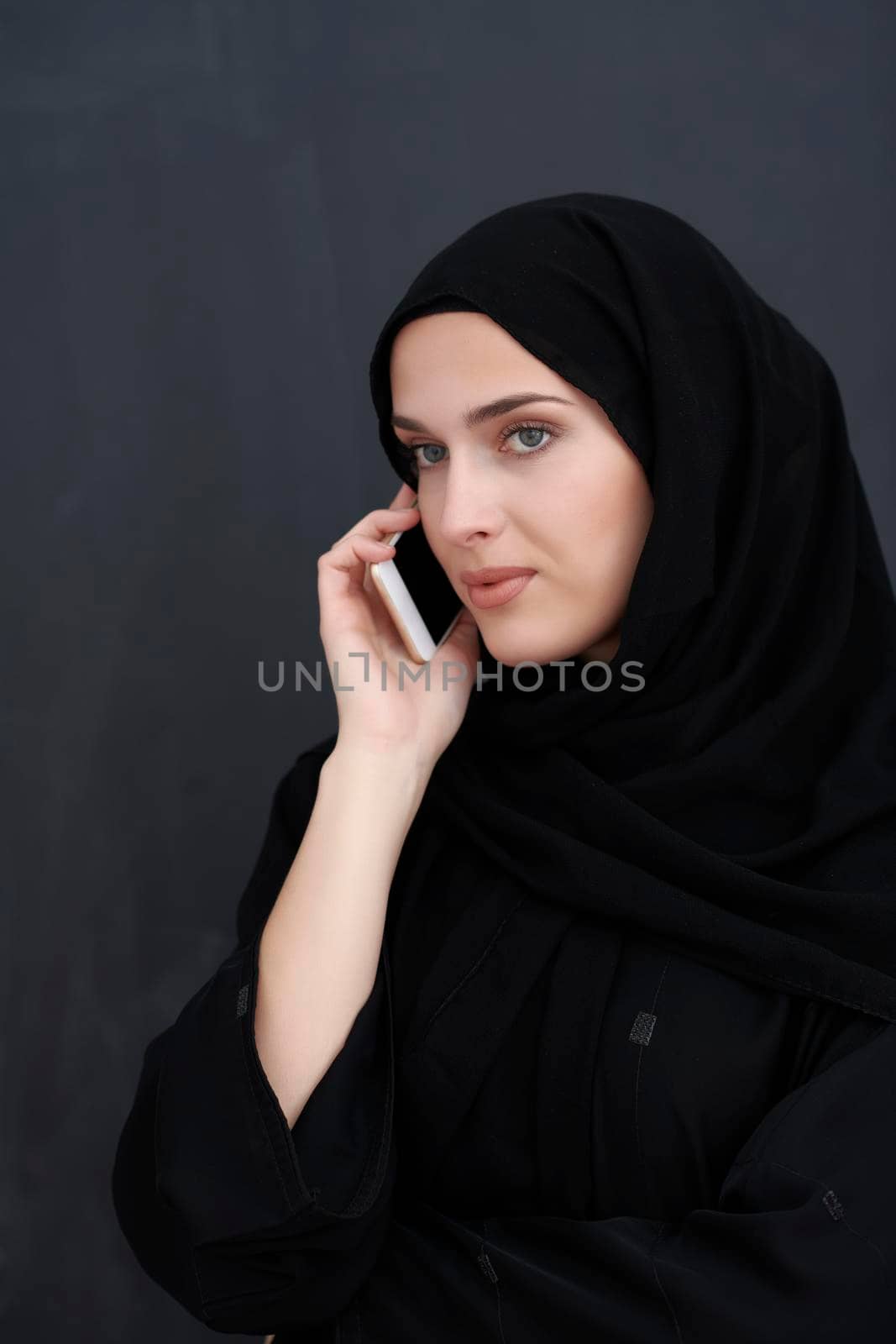 Young muslim businesswoman in traditional clothes or abaya talking on the smartphone. Arab woman  in front of black chalkboard and representing techology, islamic  fashion and Ramadan kareem concept