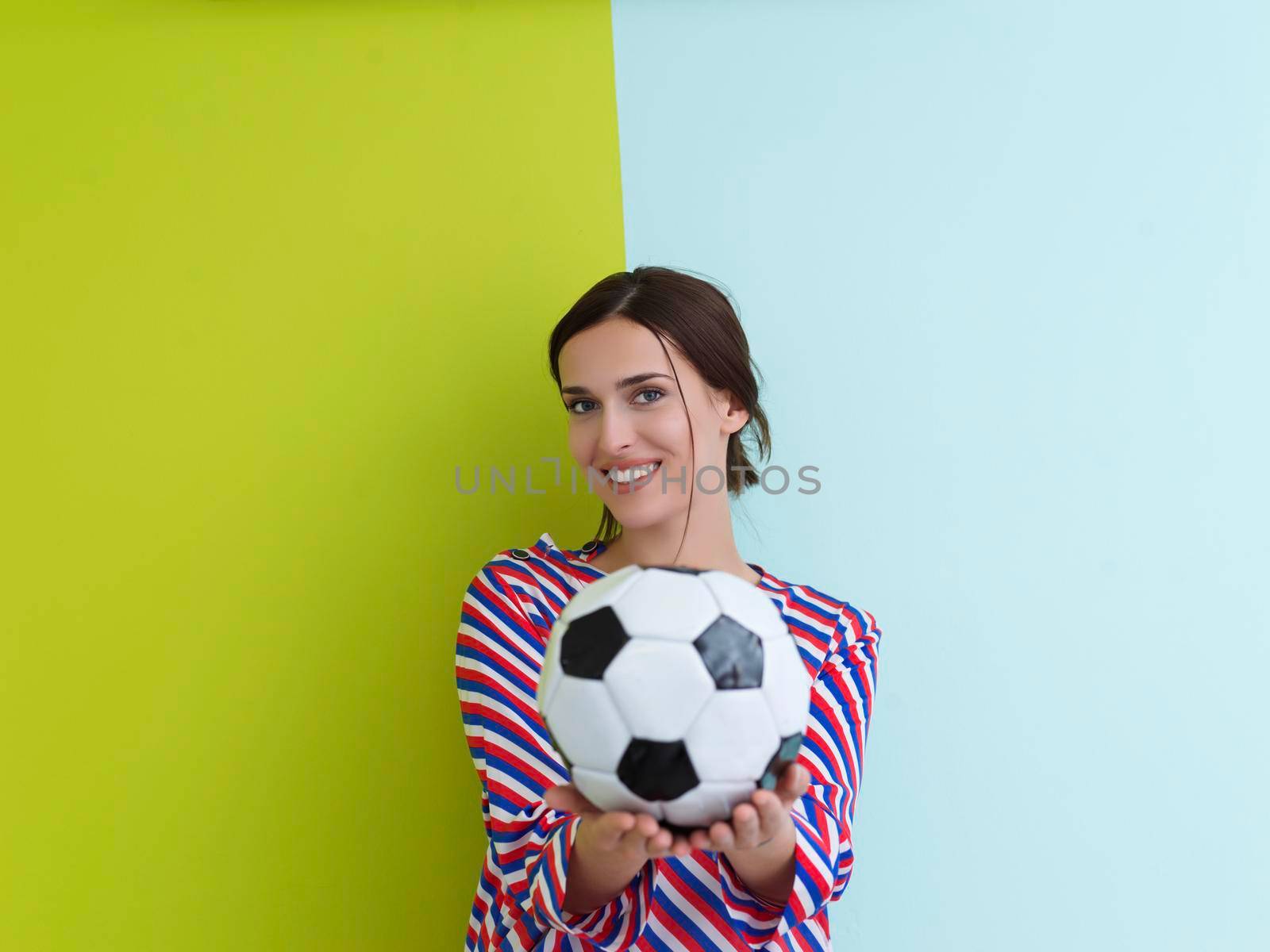 Portrait of young European woman holding soccer ball on her palm. Happy girl, football fan or player isolated on green and blue background. Sport, play football, health, healthy lifestyle concept