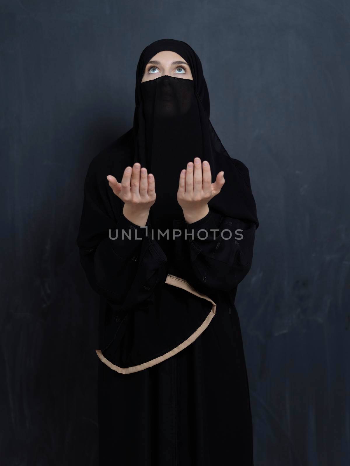 Portrait of young Muslim woman with niqab making dua. Arabian girl wearing abaya keeps hands in praying gesture. Representing worship to God and Ramadan Kareem concept