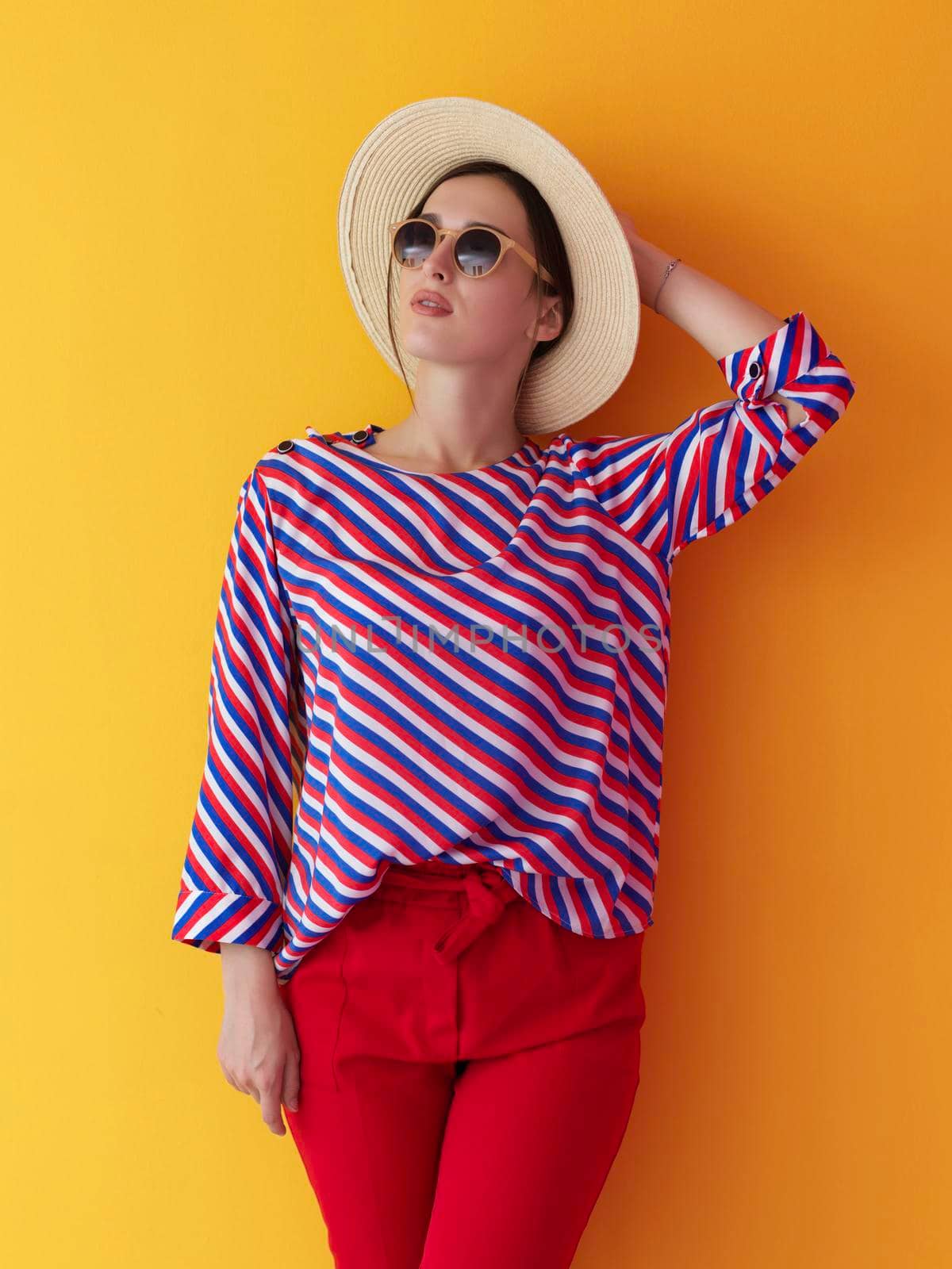 Portrait of young woman wearing sunglasses and hat over a yellow background. Female model posing in the studio. Concept of fashion