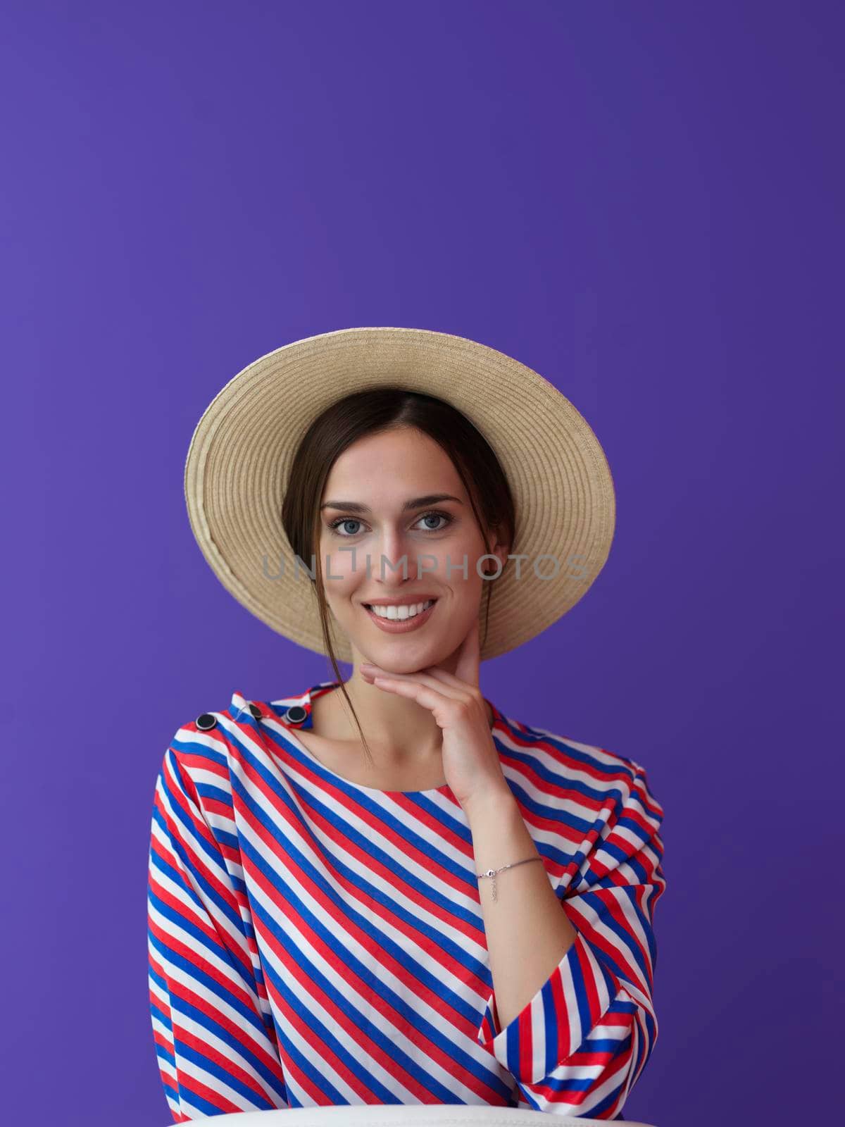 Portrait of young woman sitting on the chair isolated on purple background. Female model in casual and modern clothes posing in the studio