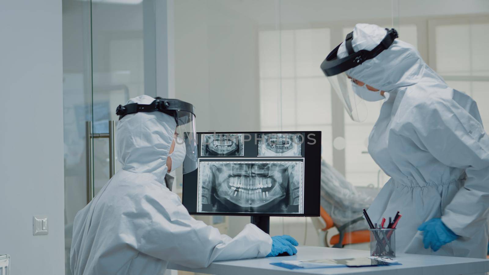 Medical dentistry staff with ppe suits using modern technology while consulting patient with oral care issues. Stomatologist and dental nurse looking at teeth animation model for implant