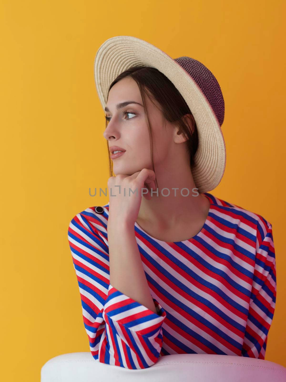 Portrait of young woman sitting on the chair isolated on yellow background. Female model in casual and modern clothes posing in the studio
