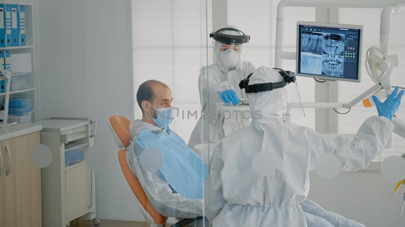 Dentistry staff wearing ppe suits doing teethcare consultation on patient, using dental equipment in stomatology cabinet. Dentist and specialist working on oral examination at clinic.