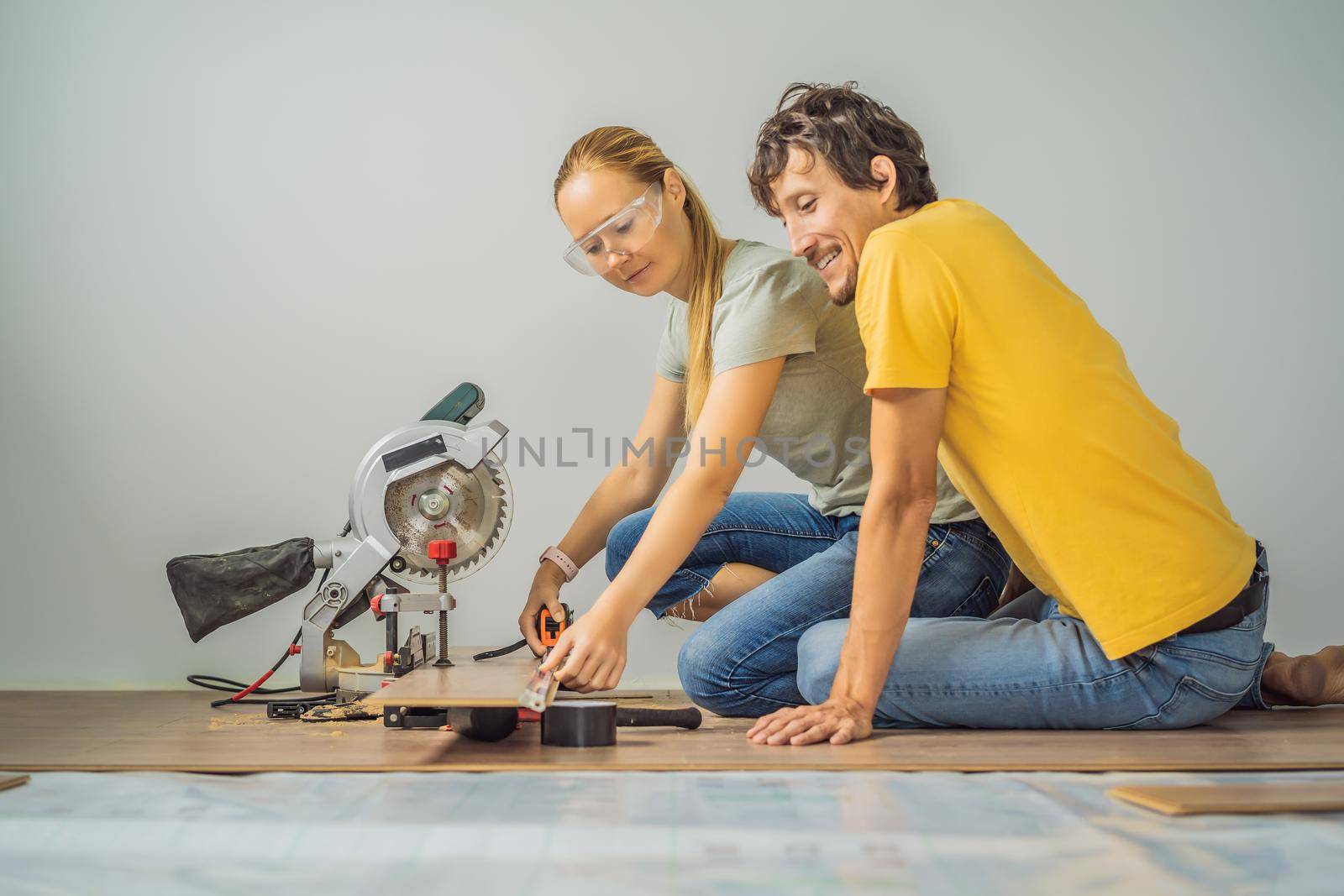 Married couple installing new wooden laminate flooring on a warm film floor. Infrared floor heating system under laminate floor.