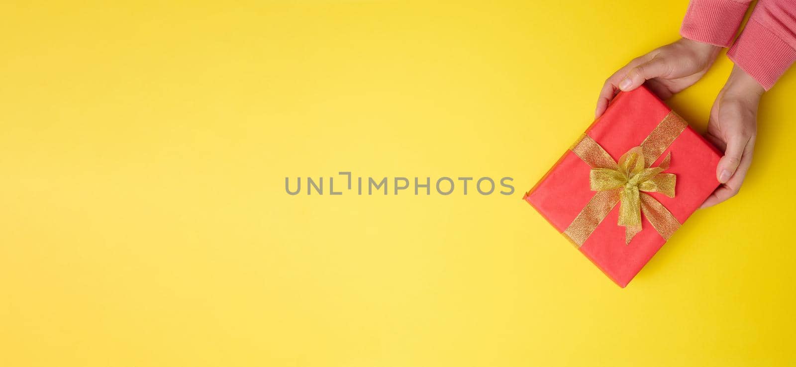 two female hands are holding red gift box on a yellow background, concept of congratulations on birthday, copy space