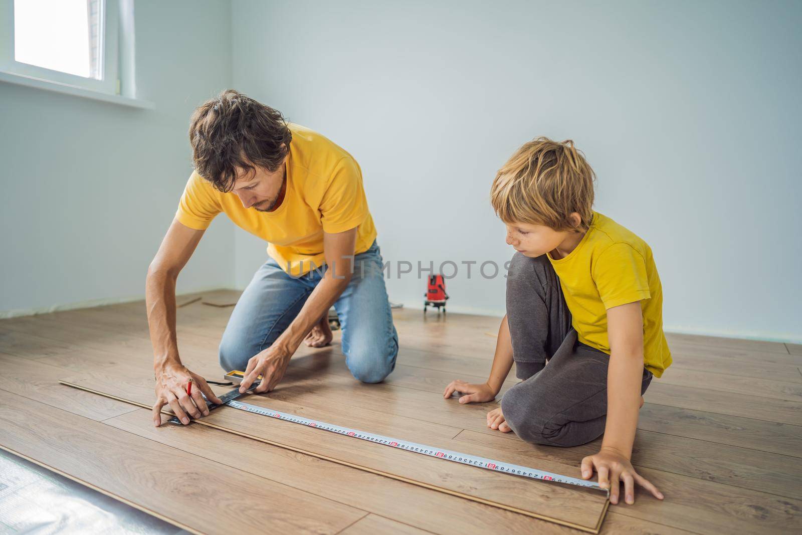 Father and son installing new wooden laminate flooring on a warm film floor. Infrared floor heating system under laminate floor.