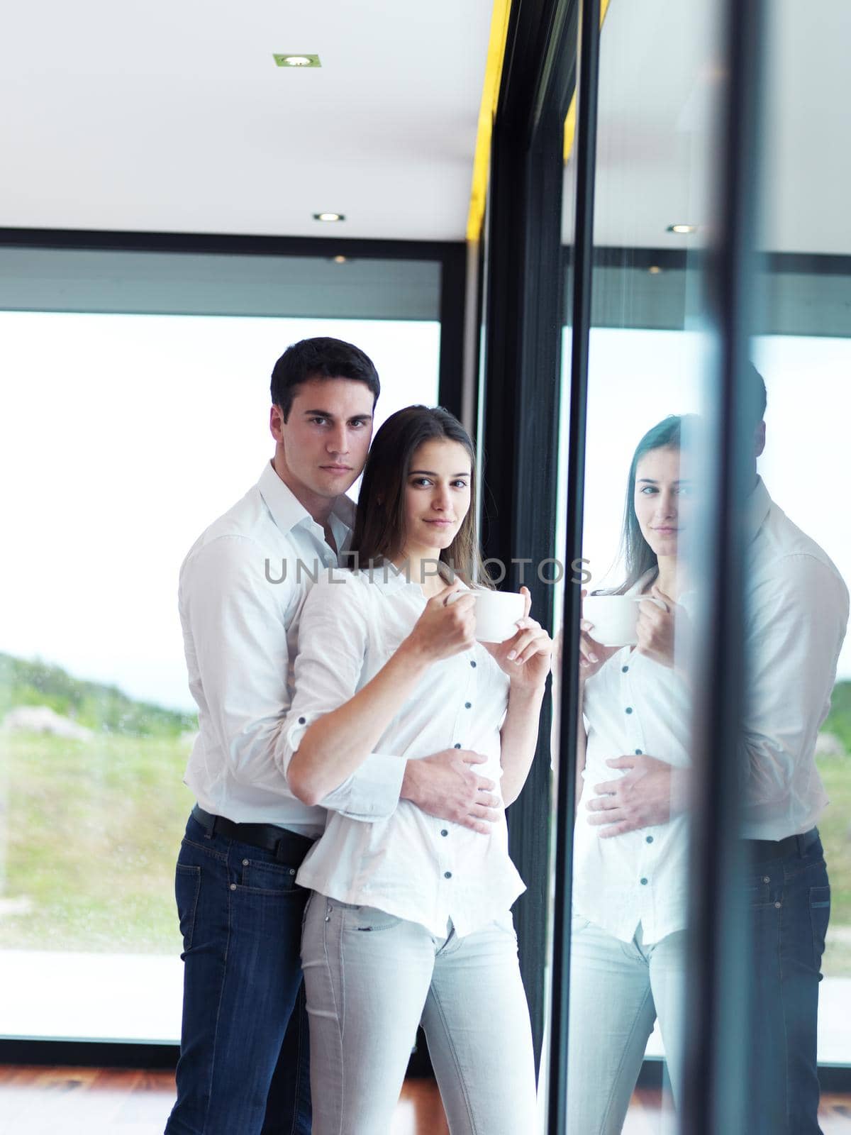 relaxet young couple drink first morning coffee  over big bright window in moder home villa indoors