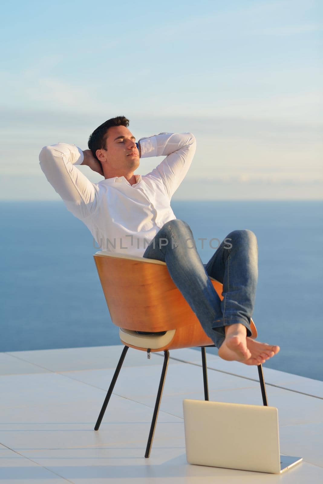 handsome young man relaxing and working on laptop computer at home balcony while looking sunset