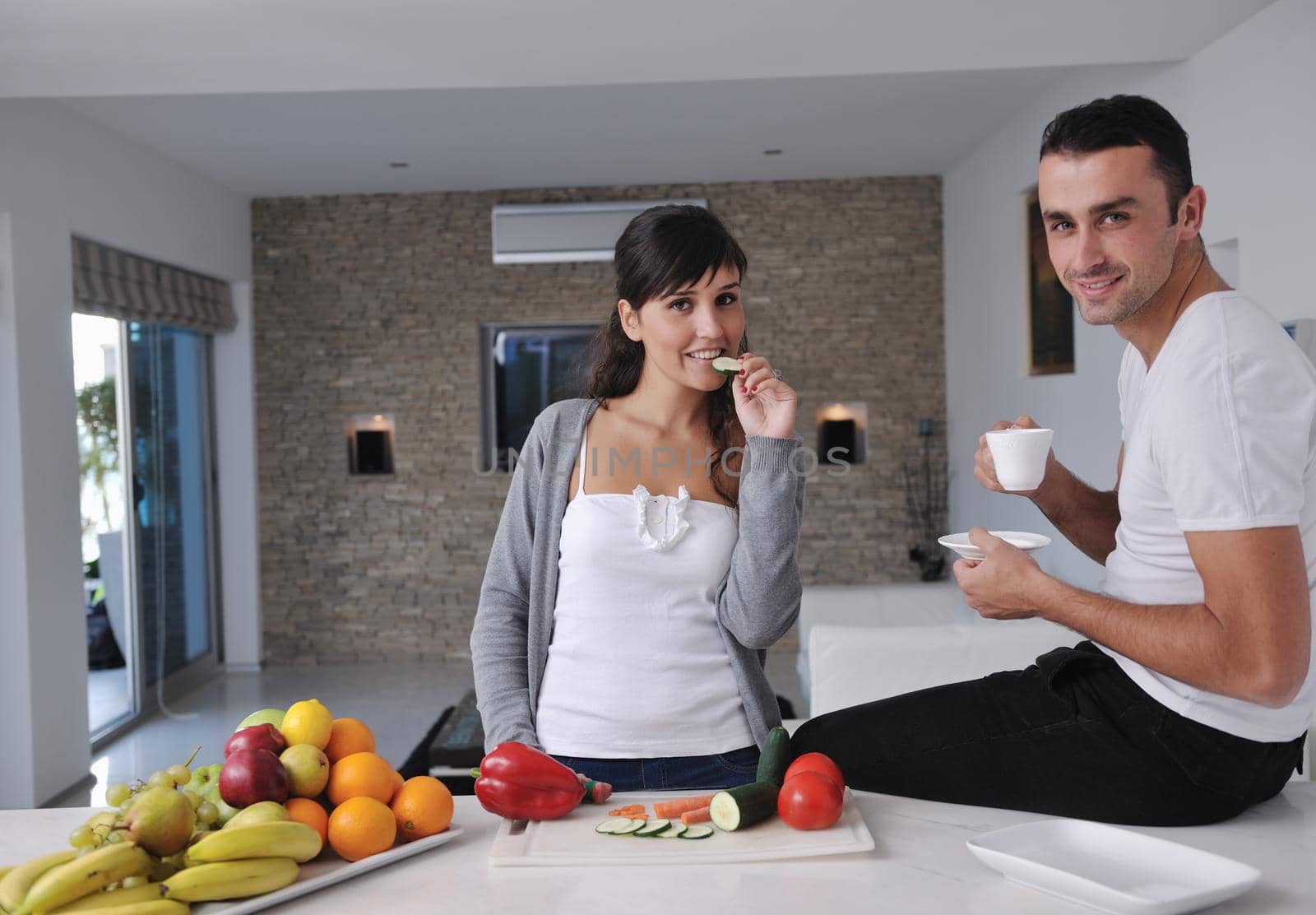 happy young couple have fun in  modern kitchen indoor  while preparing fresh fruits and vegetables food salad