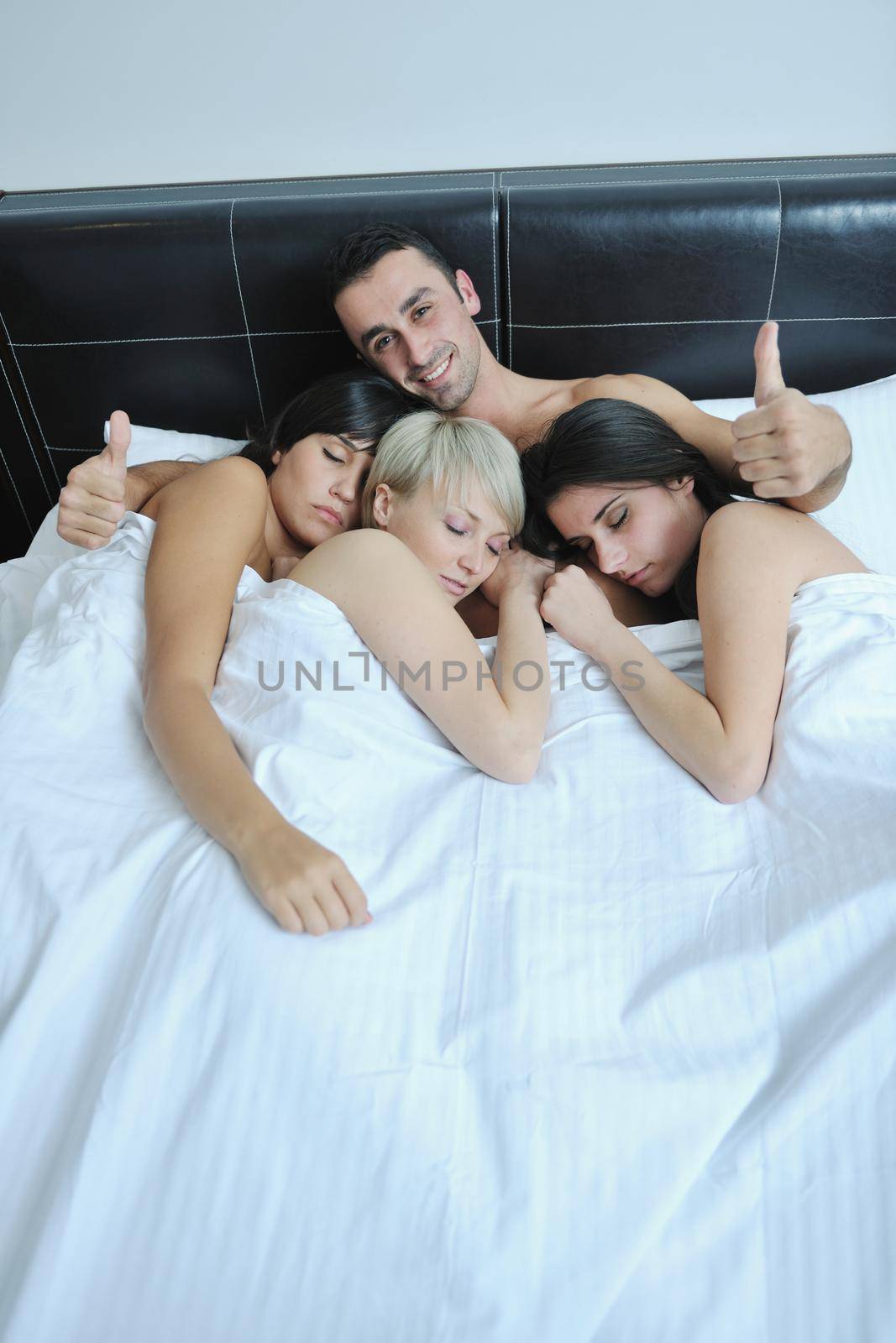 successful Young handsome man lying in bed with three sleeping girls