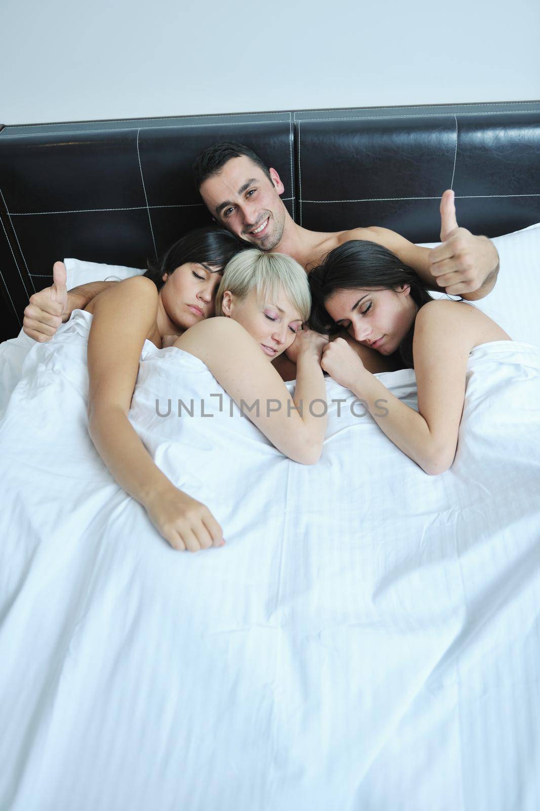 successful Young handsome man lying in bed with three sleeping girls