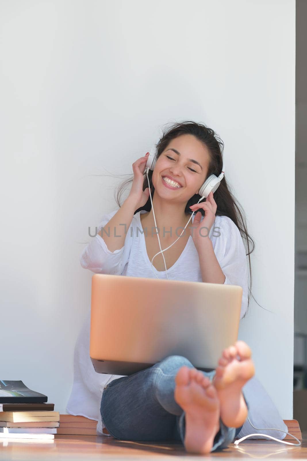 beautiful young woman relax and work on laptop computer while listening music on heaphones and read book at home