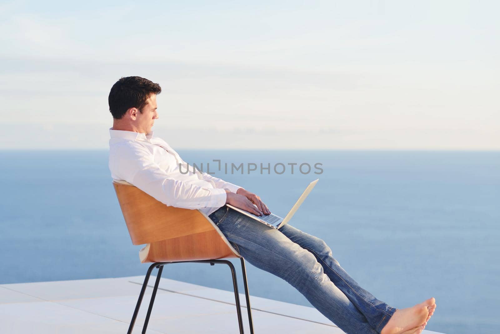 handsome young man relaxing and working on laptop computer at home balcony while looking sunset