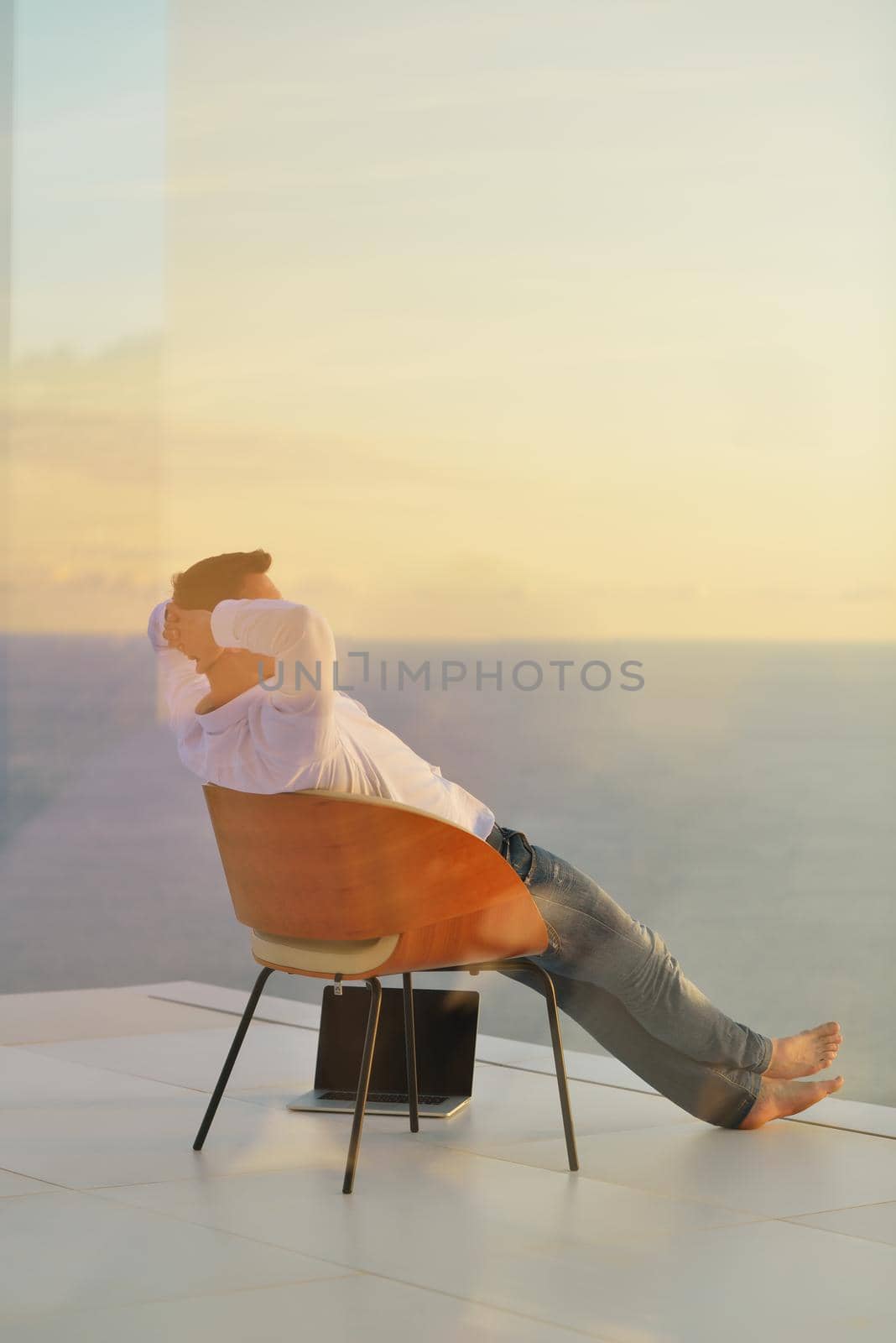 handsome young man relaxing and working on laptop computer at home balcony while looking sunset