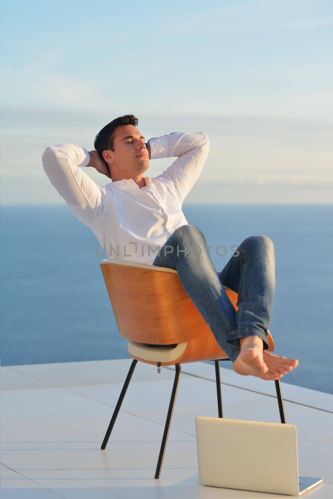 handsome young man relaxing and working on laptop computer at home balcony while looking sunset