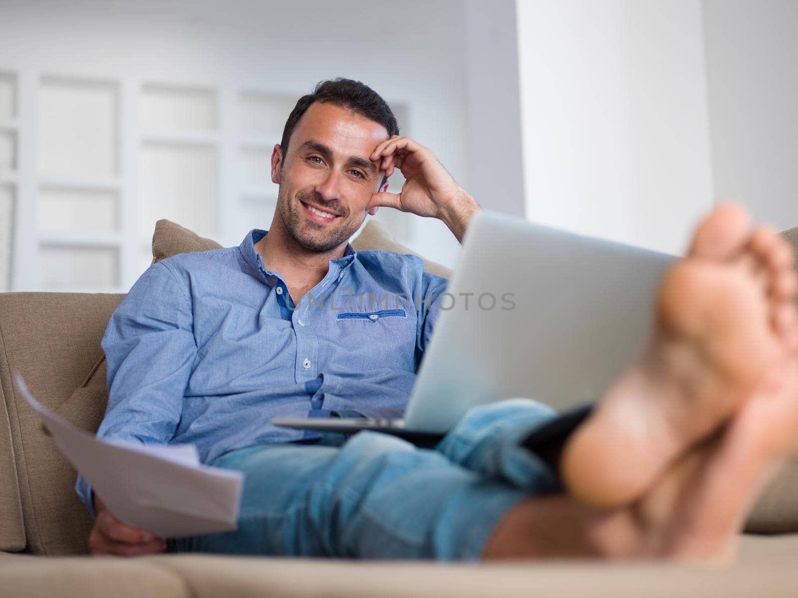 handsome young man relaxing and working on laptop computer at home balcony while looking sunset