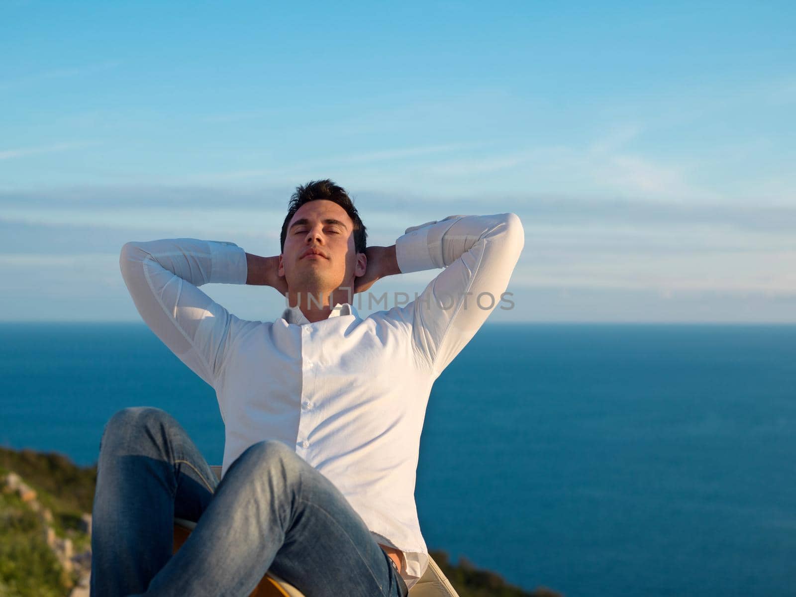 handsome young man relaxing and working on laptop computer at home balcony while looking sunset