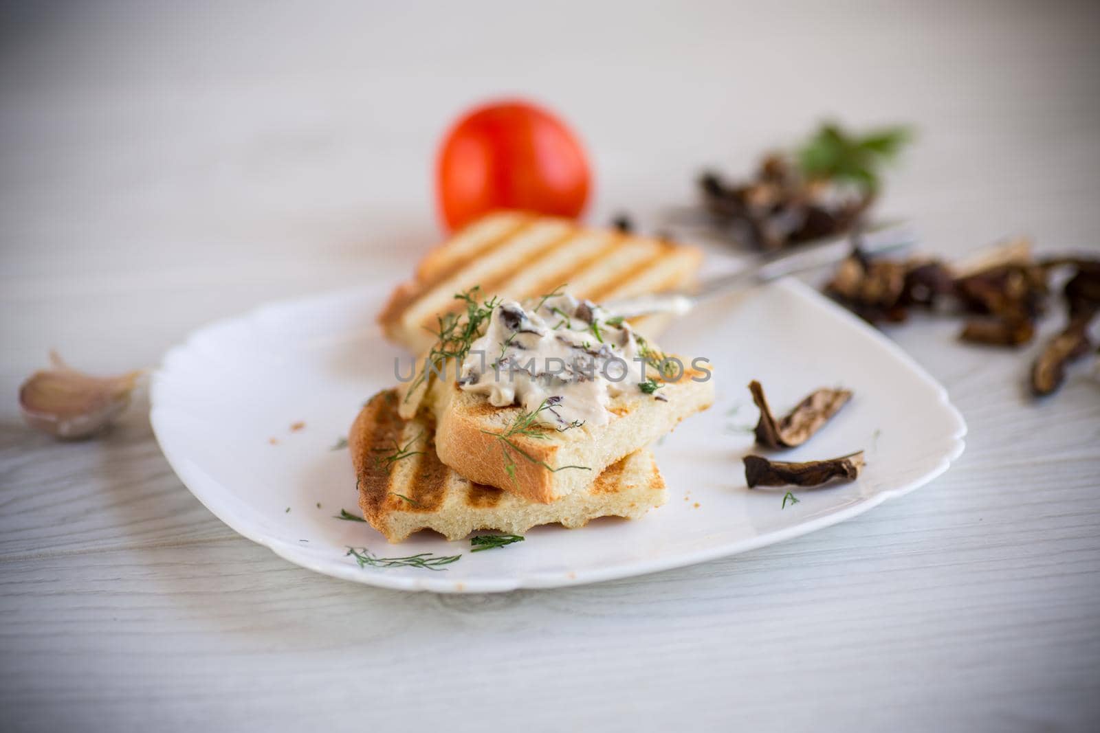 fried bread toast with cheese spread with boiled dried mushrooms, in a plate on a wooden table.