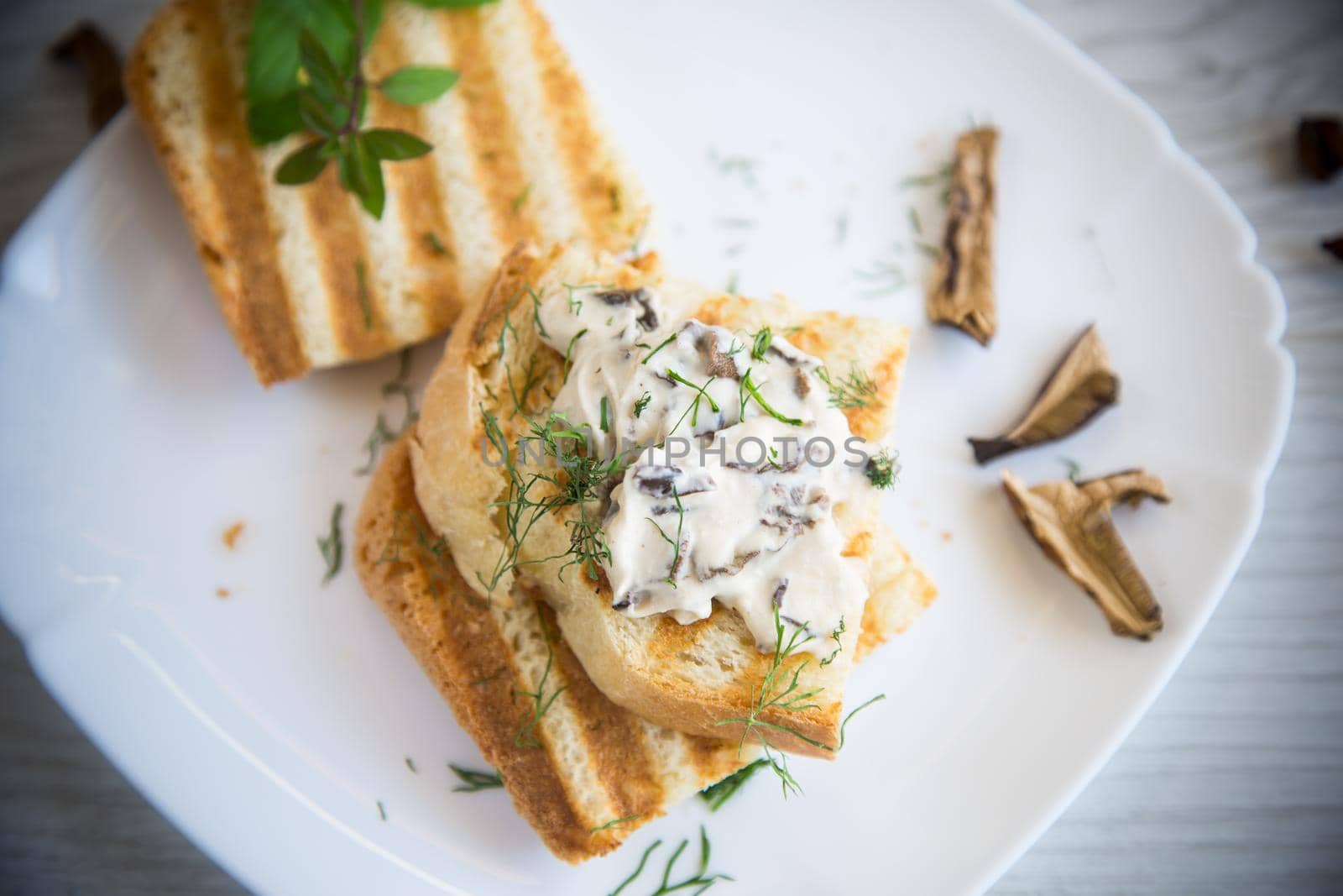 fried bread toast with cheese spread with boiled dried mushrooms, in a plate on a wooden table.