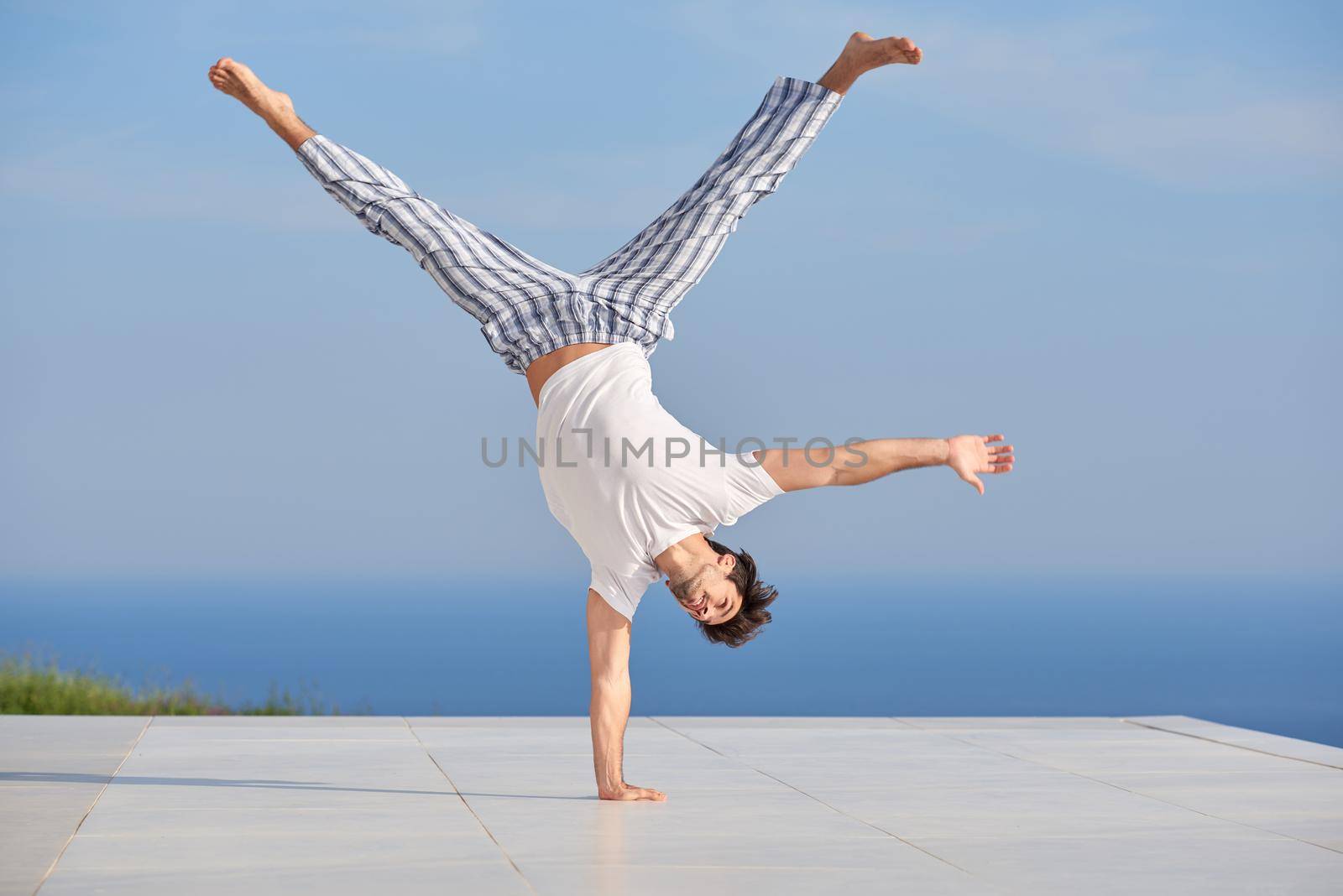 handsome young man practicing yoga on in modern home terace with ocean and sunset in background