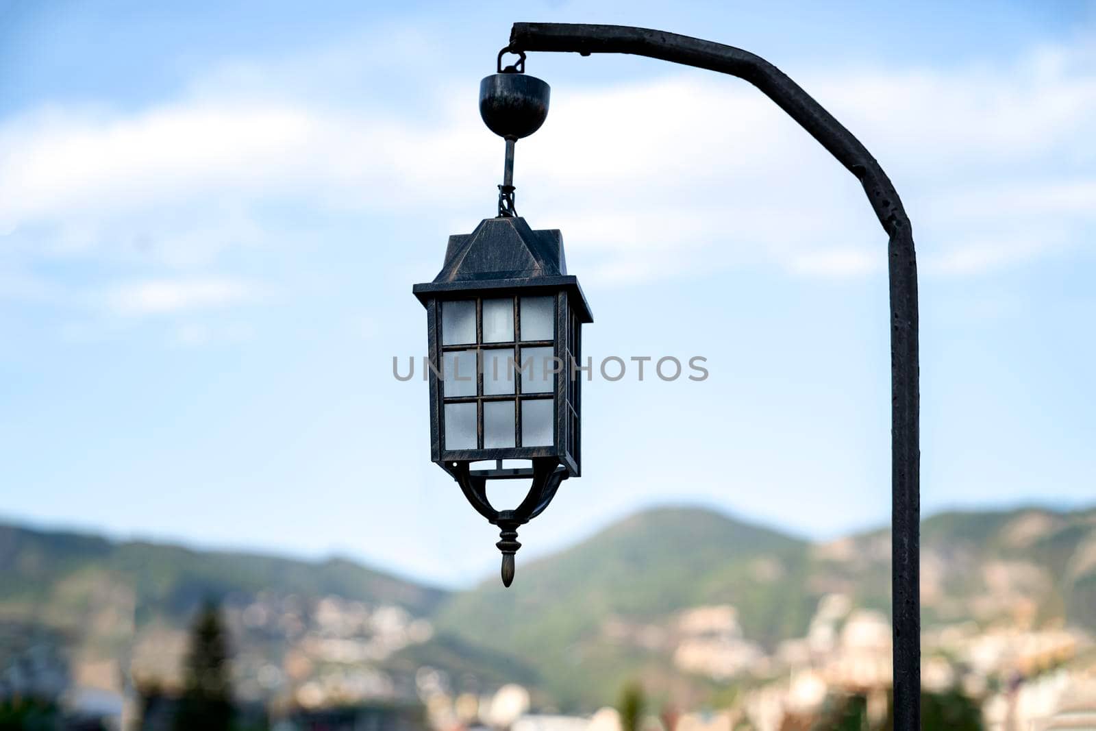 An old street lamp is hanging on a pole against the background of nature.