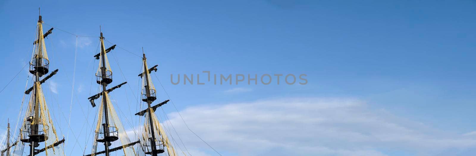 The masts of the old ship on the background of the blue sky. The concept of travel Copy space and banner