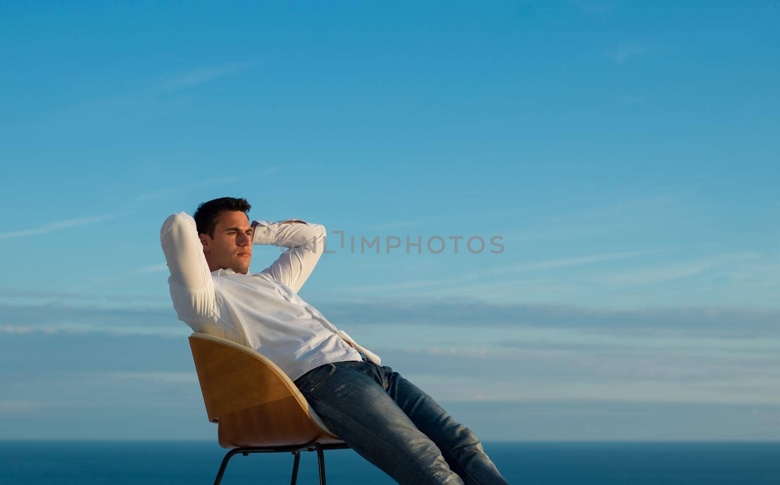 handsome young man relaxing and working on laptop computer at home balcony while looking sunset