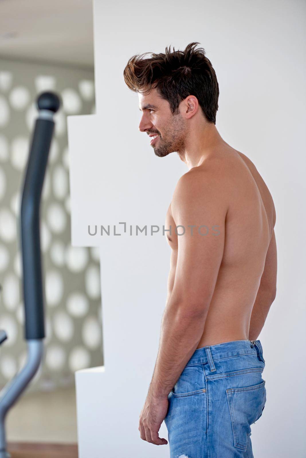 nude shirtles handsome young man in jeans posing at modern home indoors