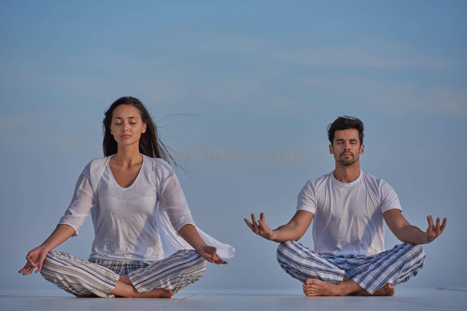 young couple practicing yoga at sunset in modern home terace with ocean and sunset in background