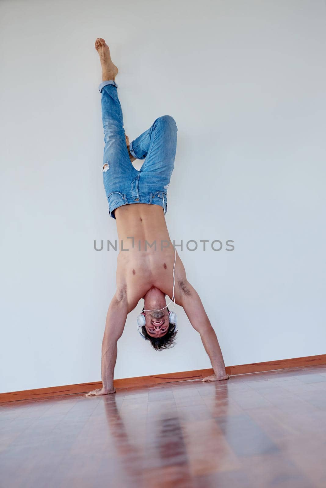 handsome young man listening music on headphones at modern home over  white wall and standing on hands