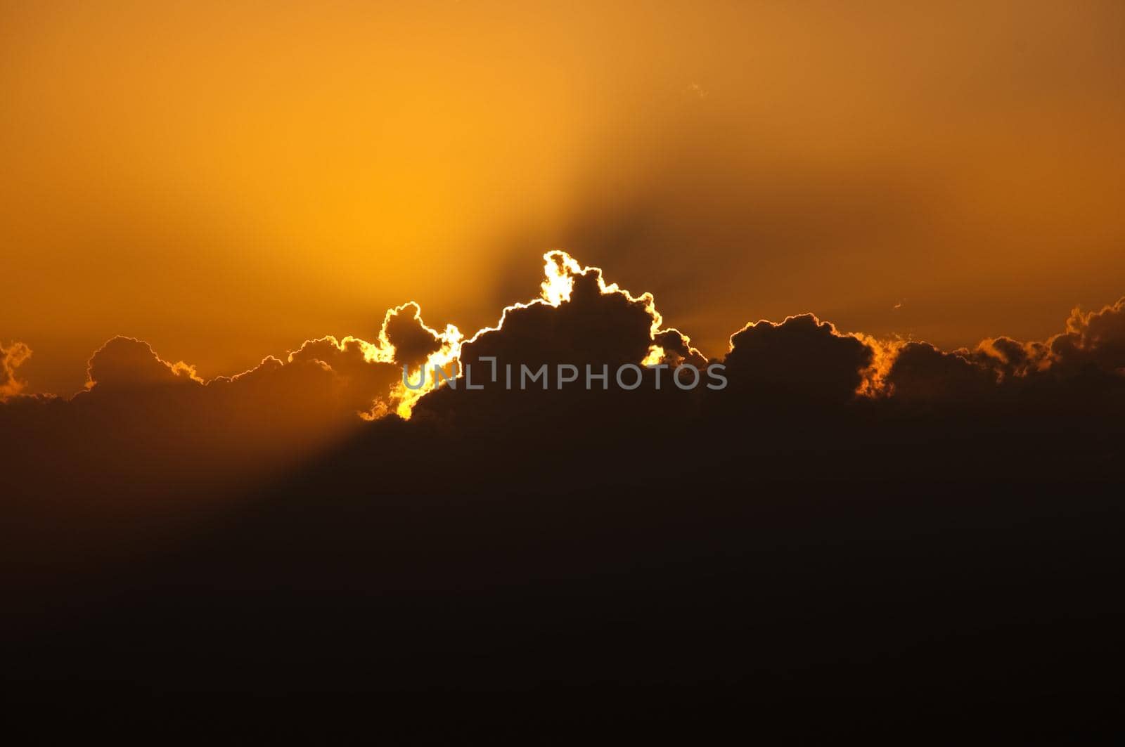 sun setting behind big cloud creating orange glow in the sky